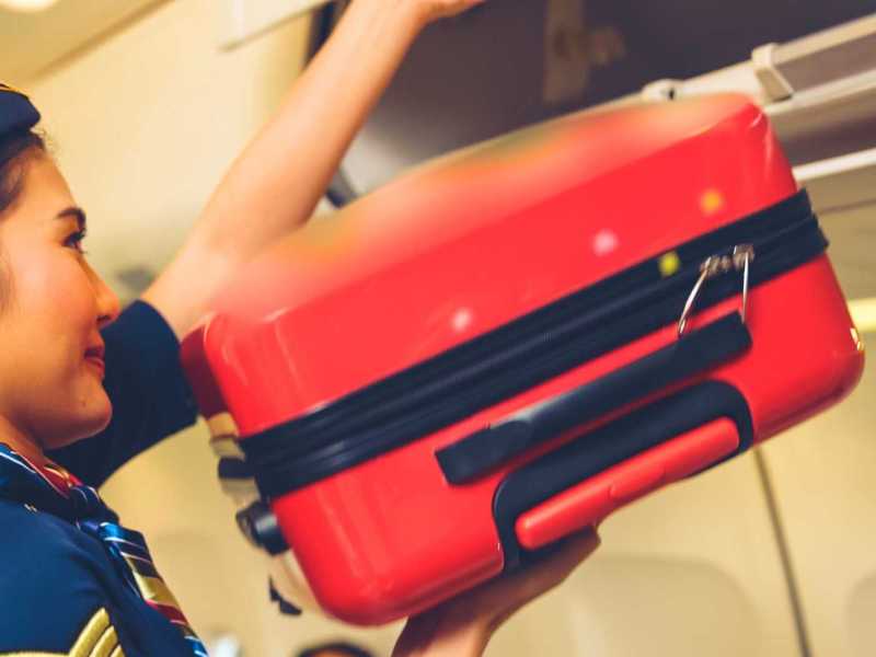 Kabinenpersonal hebt Gepäcktasche im Flugzeug