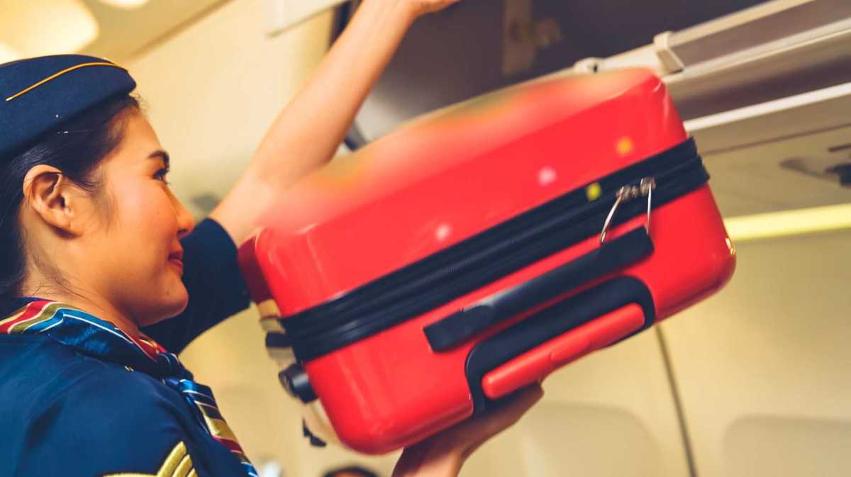 Kabinenpersonal hebt Gepäcktasche im Flugzeug