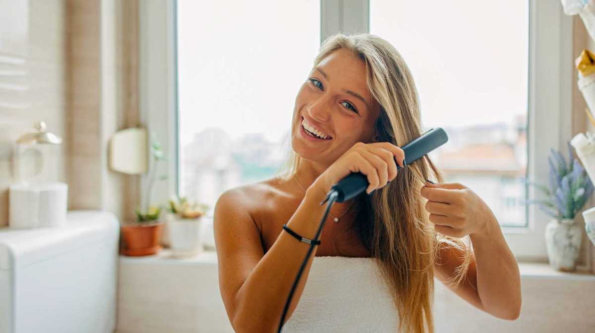 Junge Frau glättet sich die Haare.