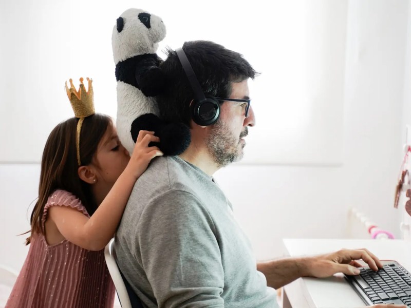 Vater am Computer, seine Tochter dahinter mit einem Pl&uuml;schtier.