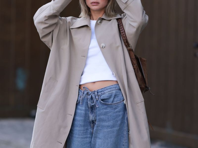 Streetstyle von Sophia Geiss in beigem Trenchcoat, weißem Crop Top und blauer Jeans mit Kordelzug