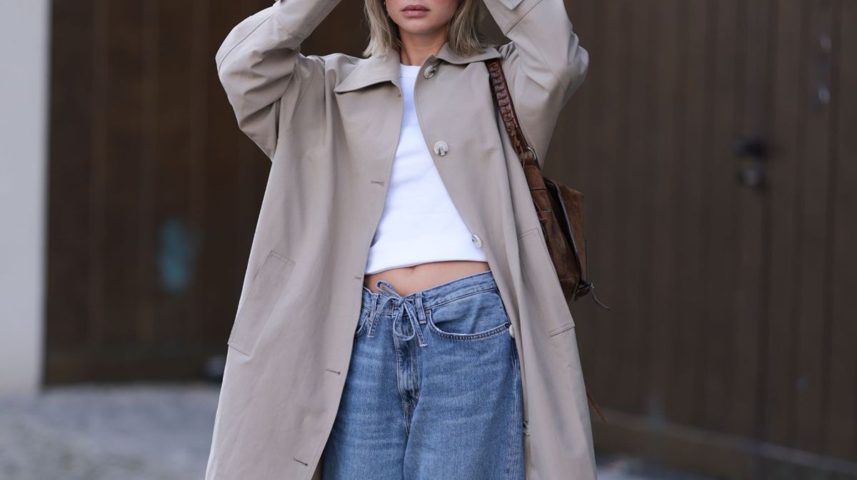 Streetstyle von Sophia Geiss in beigem Trenchcoat, weißem Crop Top und blauer Jeans mit Kordelzug
