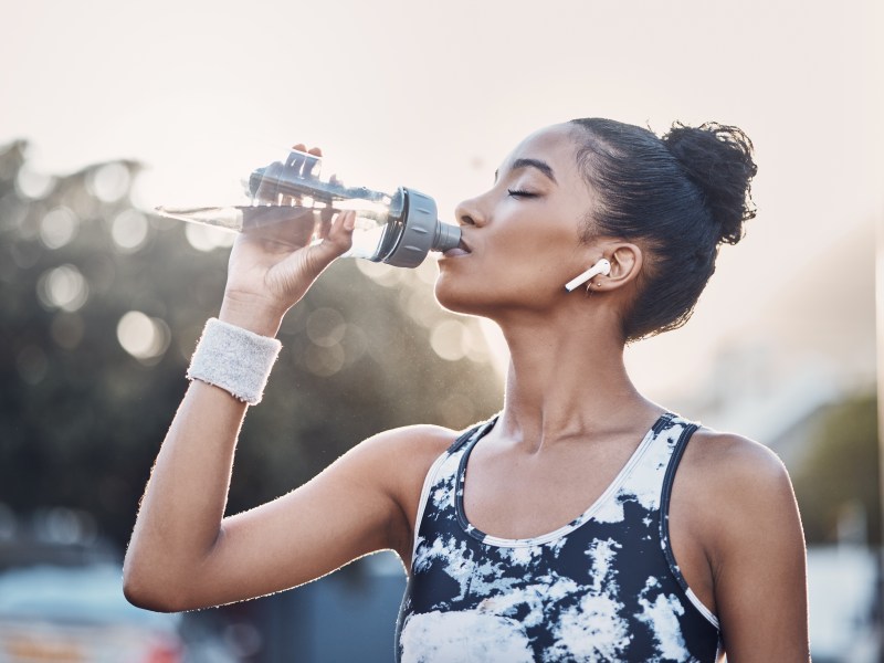 Weibliche Person, Outdoor und Übung Pause mit Flasche Wasser, städtische Umgebung und Kopfhörer für Sport Musik