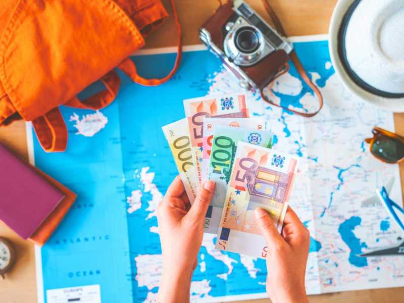 Frau hält Geld auf Reisehintergrund.