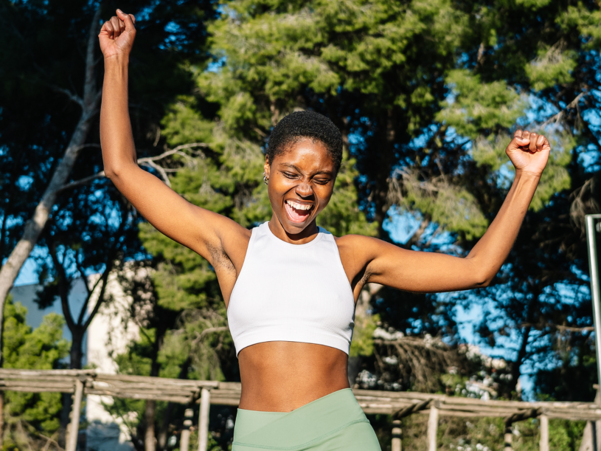 Gl&uuml;ckliche Sportlerin, die ihren Sieg in einem Park feiert und die Arme hebt