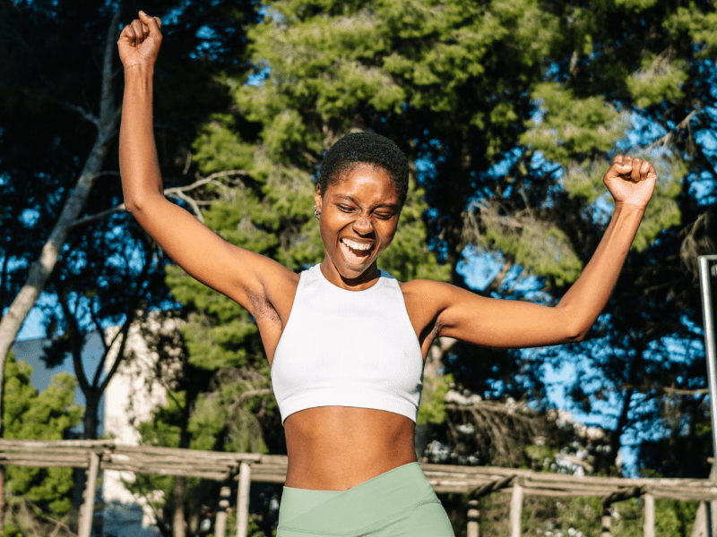 Glückliche Sportlerin, die ihren Sieg in einem Park feiert und die Arme hebt