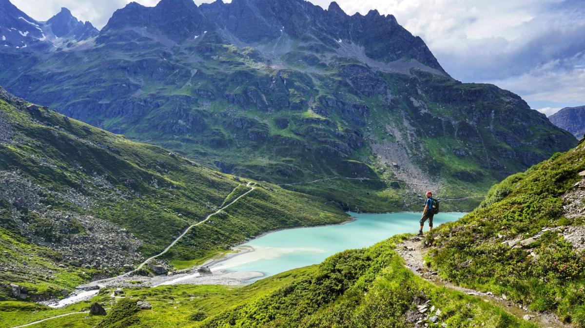 Wanderer steht vor einer Bergkulisse und einem Bergsee.