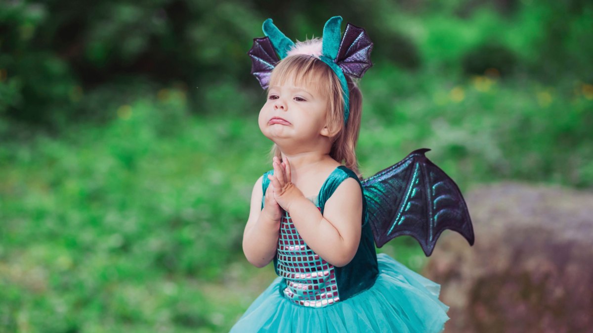 Kleines Mädchen im Drachenkostüm steht im Wald und bettelt um etwas, das es haben möchte.