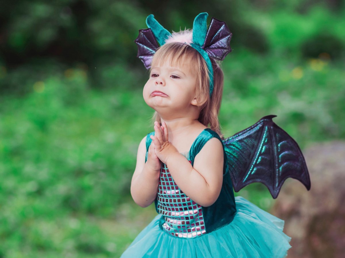Kleines Mädchen im Drachenkostüm steht im Wald und bettelt um etwas, das es haben möchte.