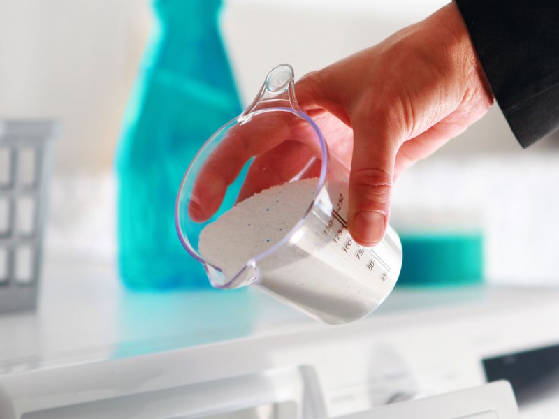 Hand, die Waschmittel in Waschmaschinenfach einfüllt