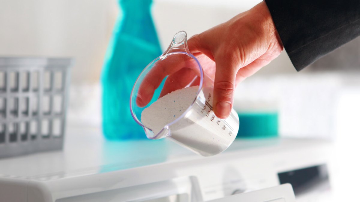 Hand, die Waschmittel in Waschmaschinenfach einfüllt