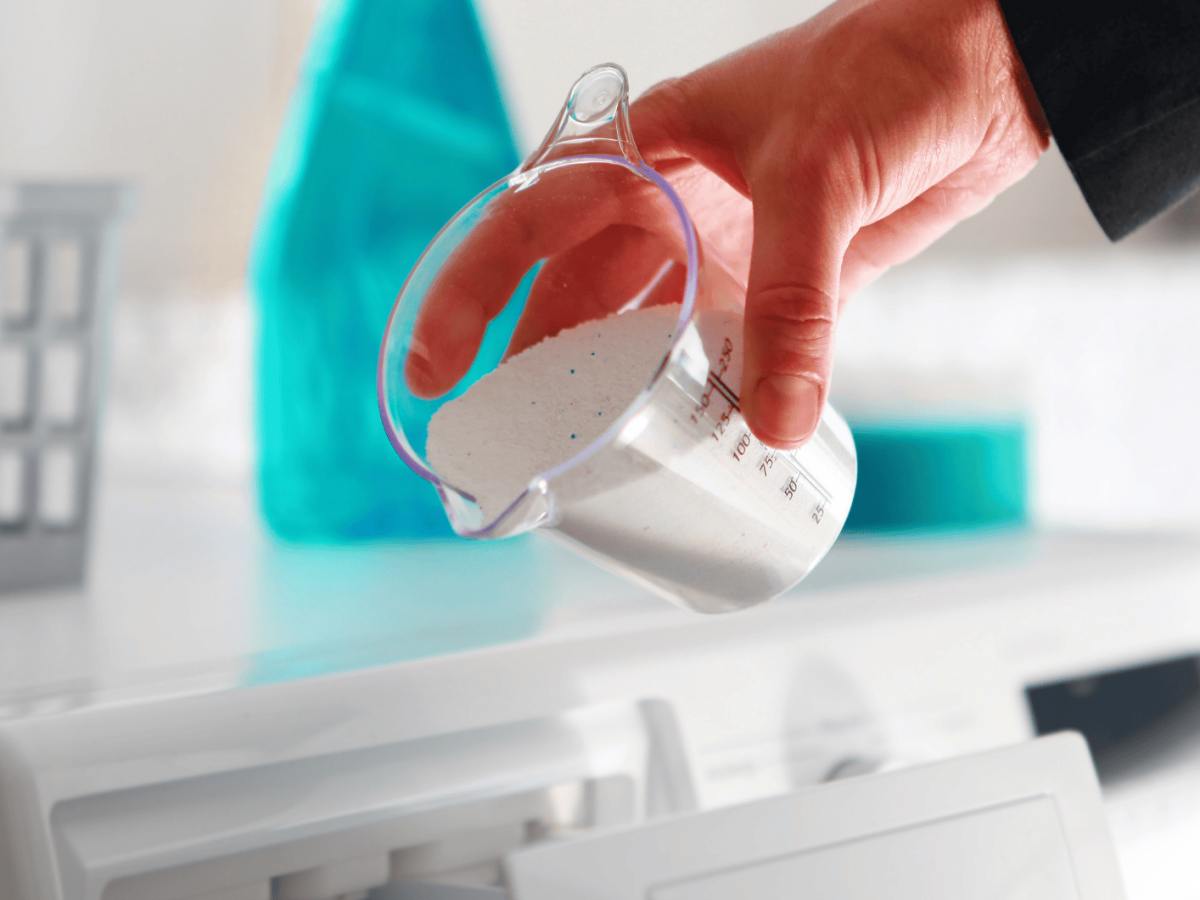 Person schüttet Waschmittel in Waschmaschine.