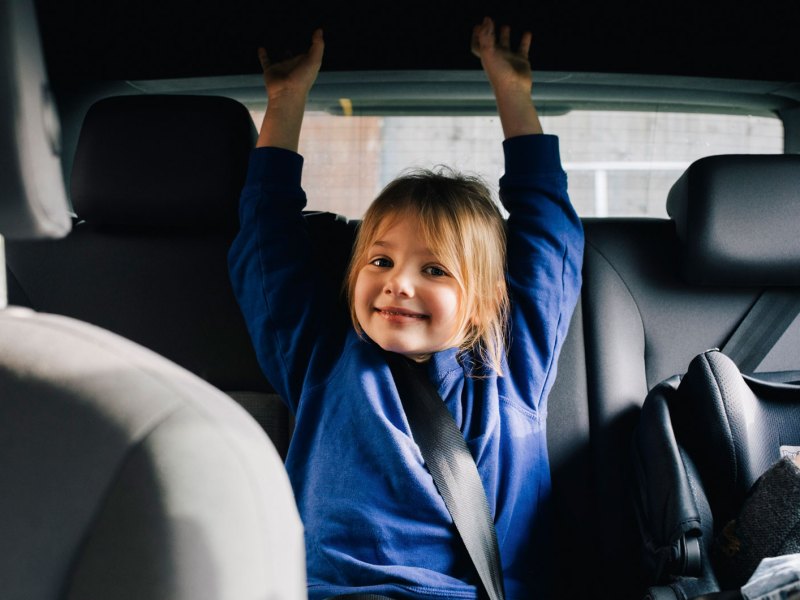 Mädchen auf der Rückbank im Auto lacht freundlich in die Kamera.