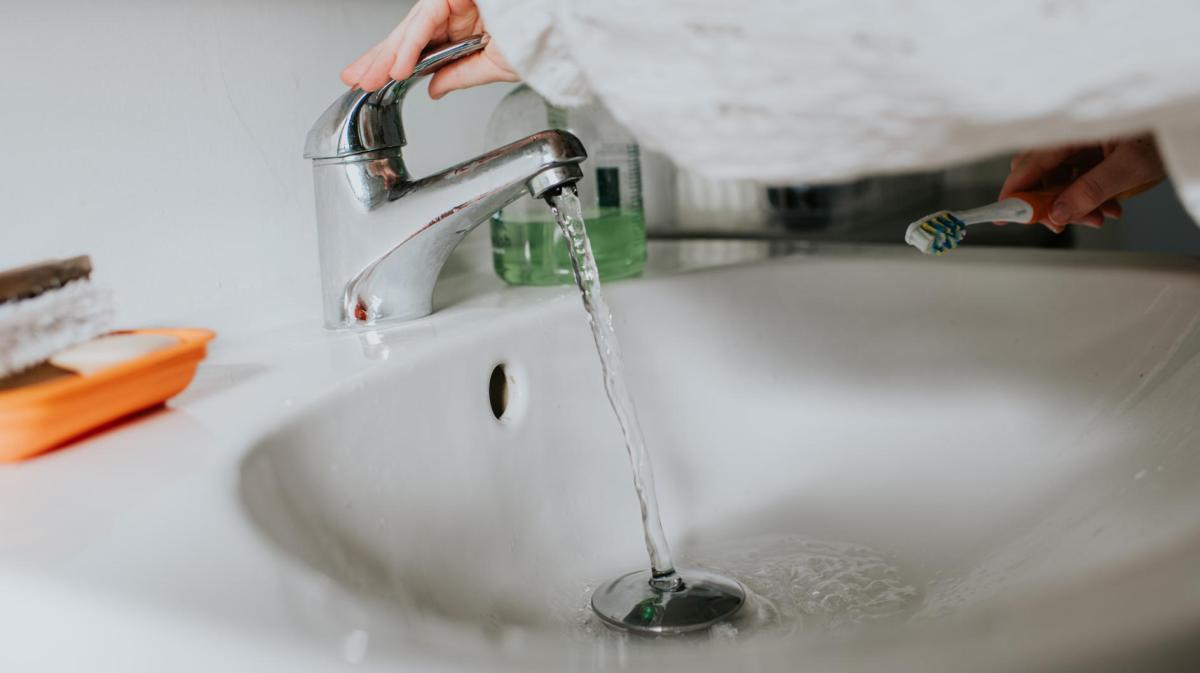 Frau dreht Wasserhahn an einem Waschbecken auf.