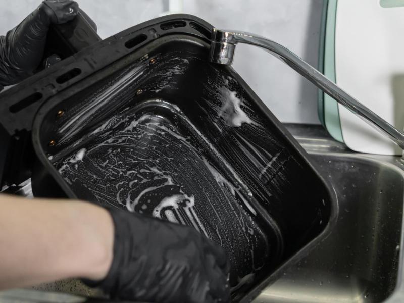 Person macht die Schublade eines Airfryers im Spülbecken mit einem Schwamm sauber.