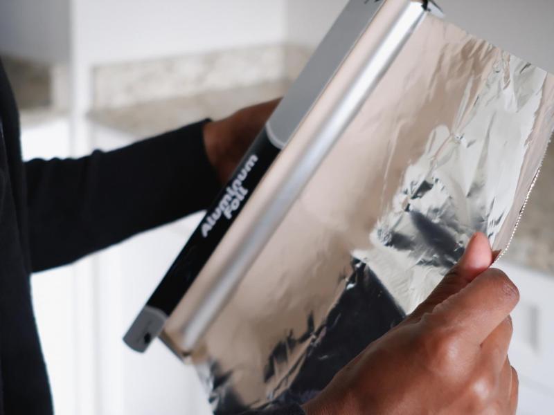 Frau reißt Alufolie von einer Rolle.