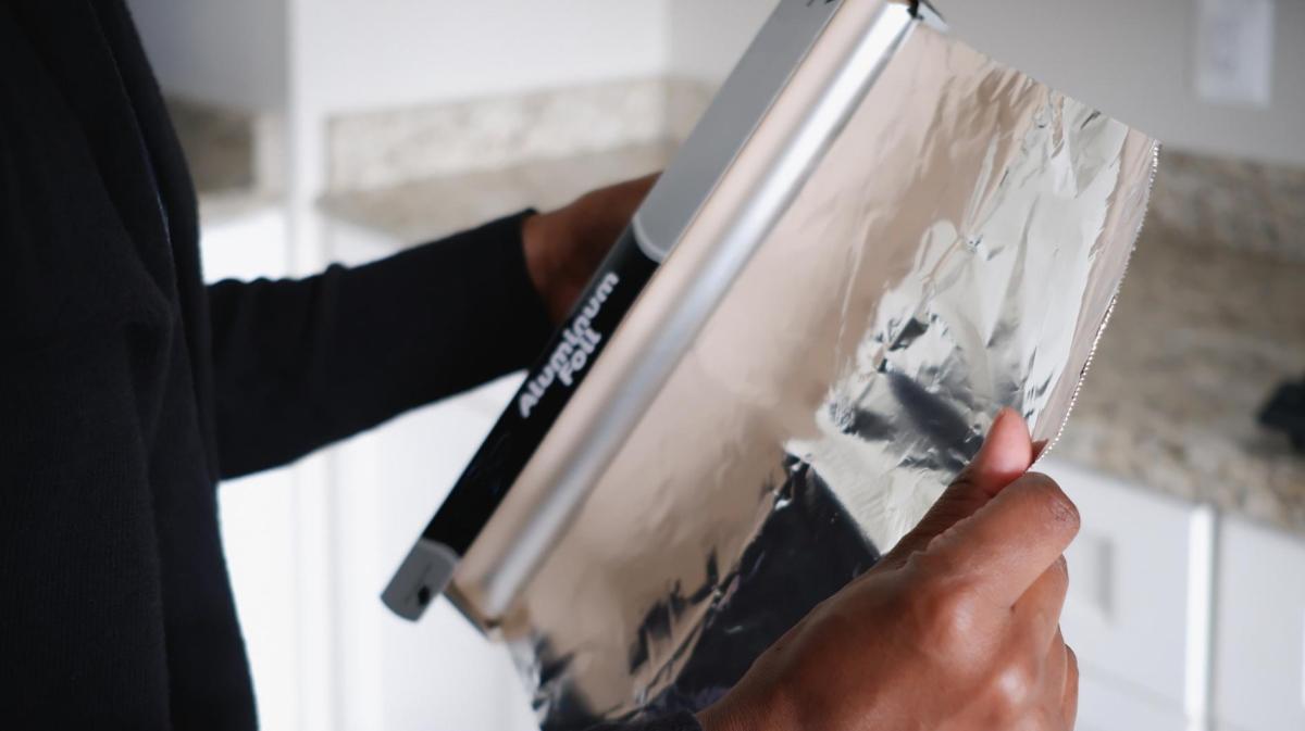 Frau reißt Alufolie von einer Rolle.