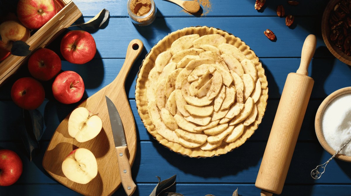 Ungebackener hausgemachter Apfelkuchen und Zutaten auf blauem Holztisch, flach liegen