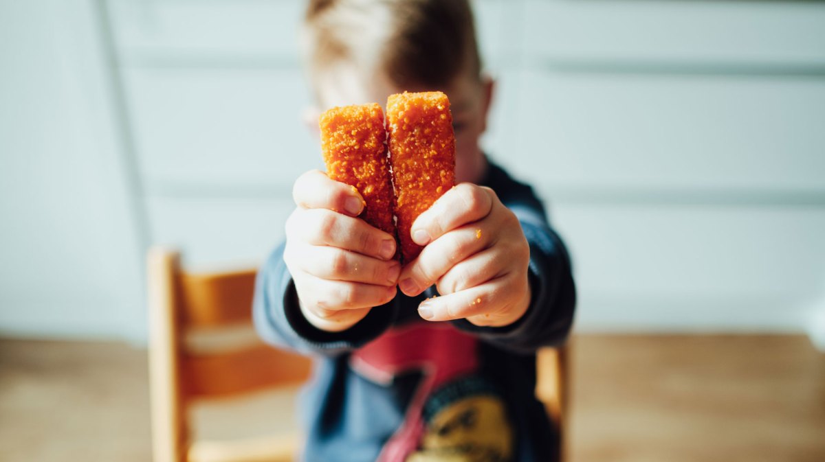 Kind hält zwei Fischstäbchen in die Kamera.