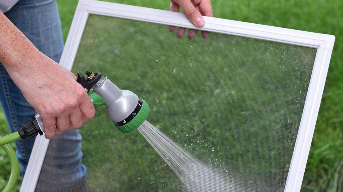 Person duscht Fliegengitter mit einem Wasserschlauch im Garten ab.