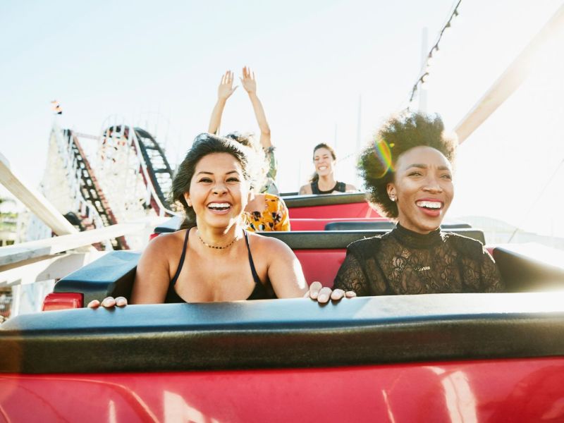 Zwei Frauen sitzen in einer Achterbahn und freuen sich.