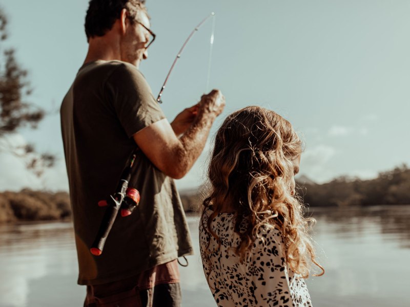 Vater und Tochter stehen am See und bereiten eine Angel vor.