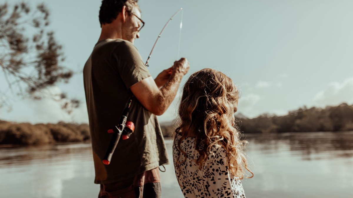 Vater und Tochter stehen am See und bereiten eine Angel vor.