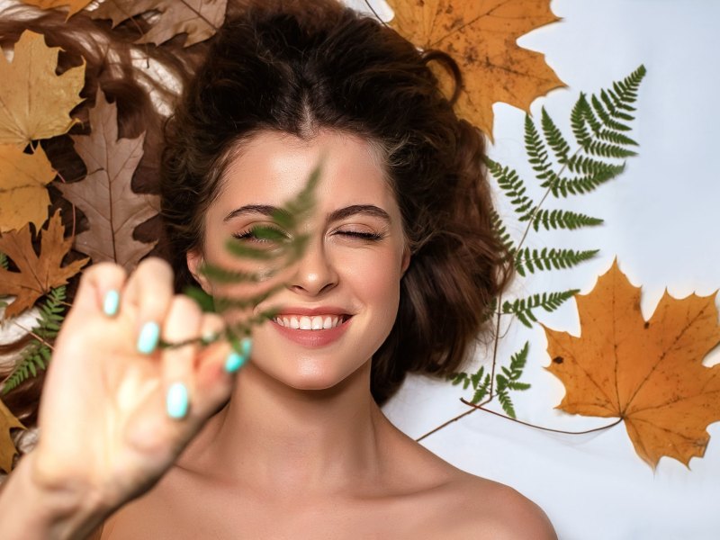 Frau mit einem strahlenden Teint, die auf herbstlichem Laub liegt.