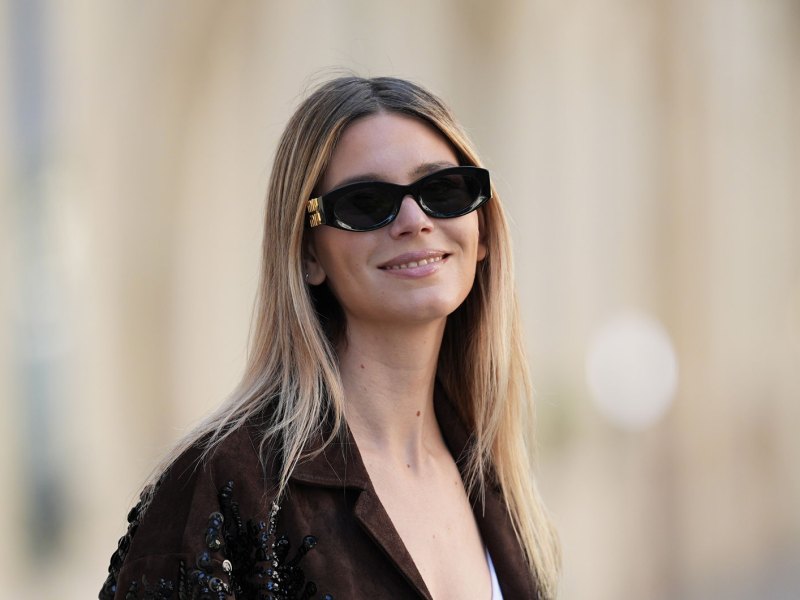 Lächelnde Frau im Herbst mit einer brauen Jacke.