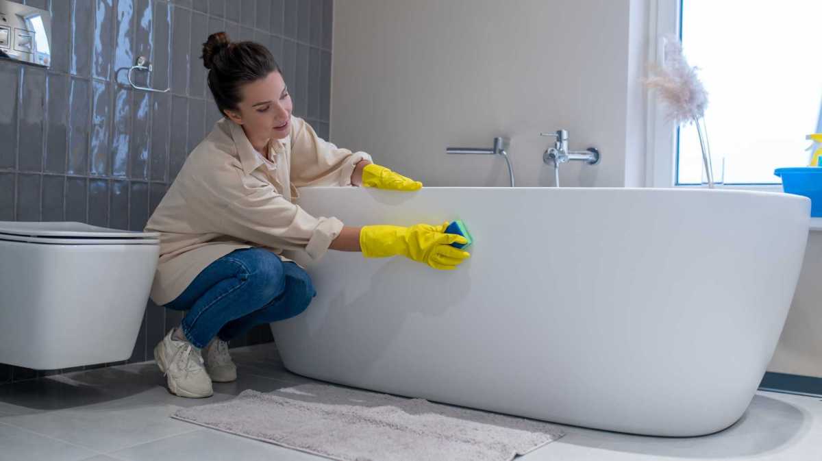 Frau putzt Badewanne mit einem Schwamm