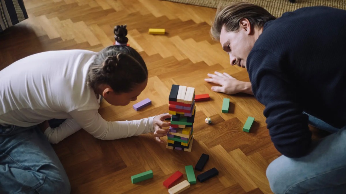 Vater und Tochter spielen Jenga auf dem Fußboden.