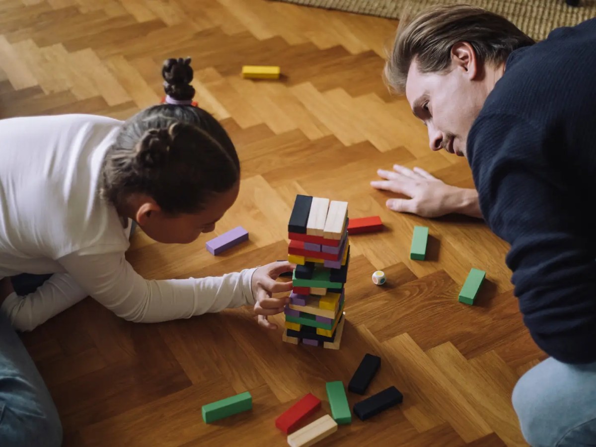 Vater und Tochter spielen Jenga auf dem Fußboden.