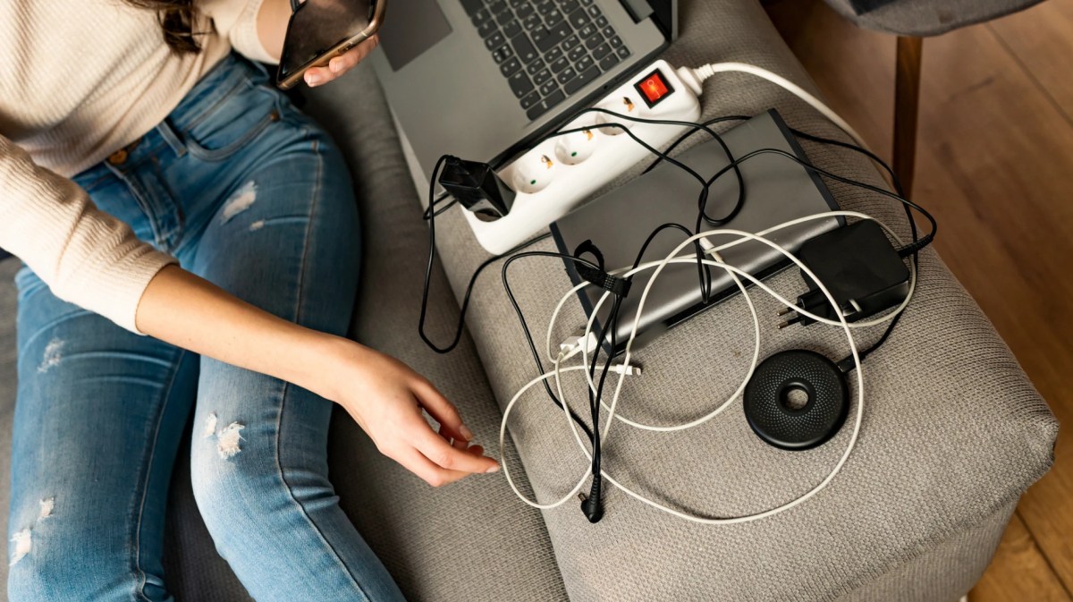 Eine Frau sitzt auf dem Sofa, neben ihr viele Elektrogeräte mit Ladekabeln