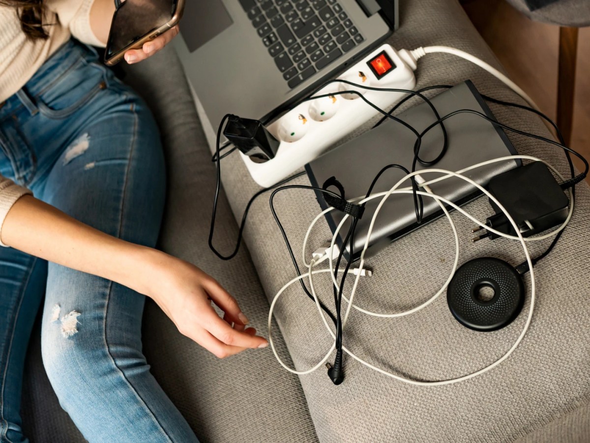 Eine Frau sitzt auf dem Sofa, neben ihr viele Elektrogeräte mit Ladekabeln