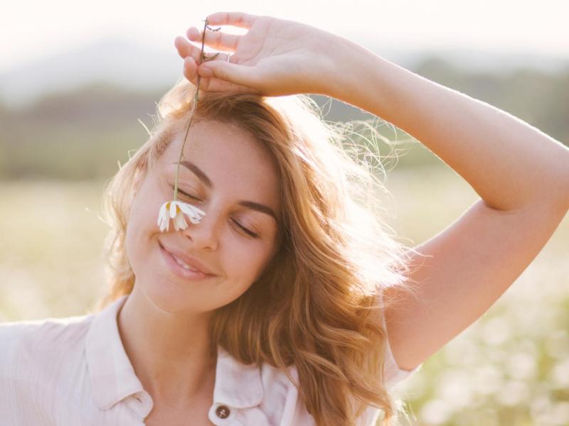 Junge Frau läuft mit einer Blume über eine Wiese.