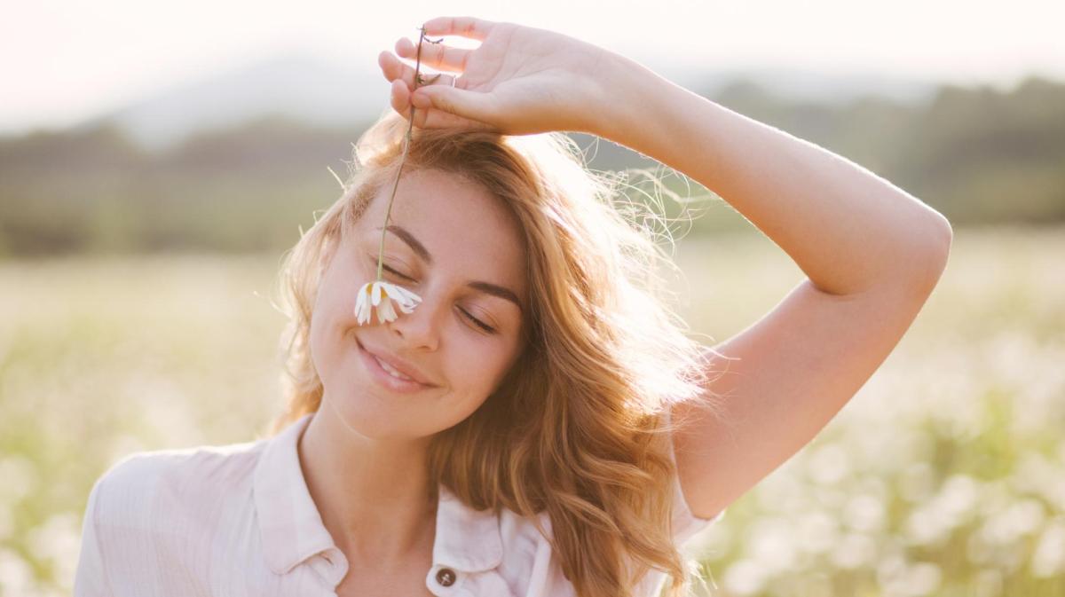 Junge Frau läuft mit einer Blume über eine Wiese.