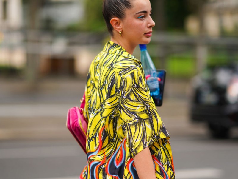 PARIS, FRANCE - JUNE 18: A guest wears earrings, a hot pink bag, a yellow bananas pattern Prada shirt, outside Heron Preston, during Paris Fashion Week - Menswear Spring/Summer 2020, on June 18, 2019 in Paris