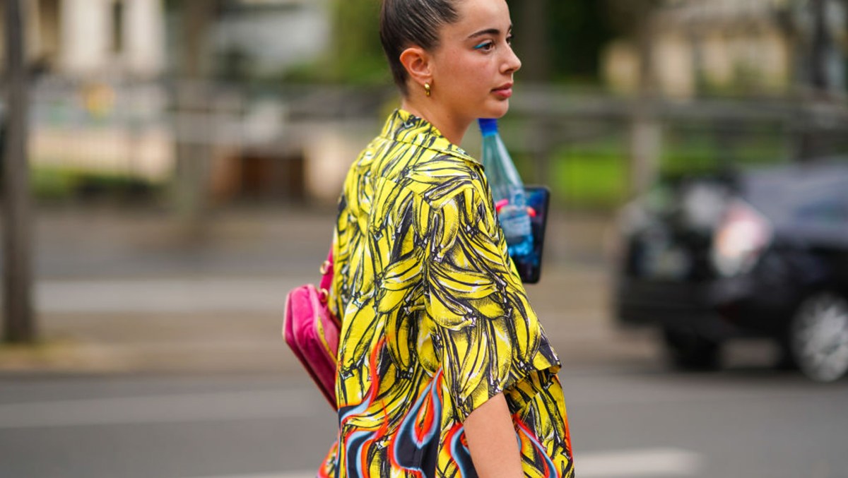 PARIS, FRANCE - JUNE 18: A guest wears earrings, a hot pink bag, a yellow bananas pattern Prada shirt, outside Heron Preston, during Paris Fashion Week - Menswear Spring/Summer 2020, on June 18, 2019 in Paris