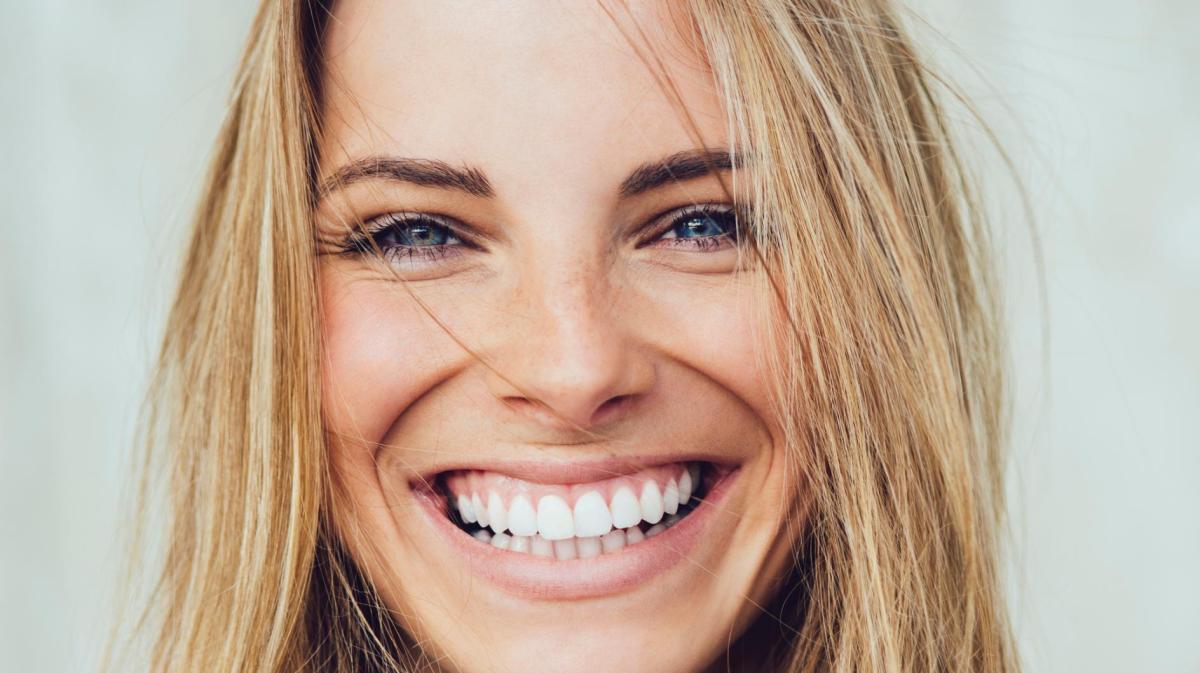 Junge blonde Frau mit blauen Augen strahlt in die Kamera.