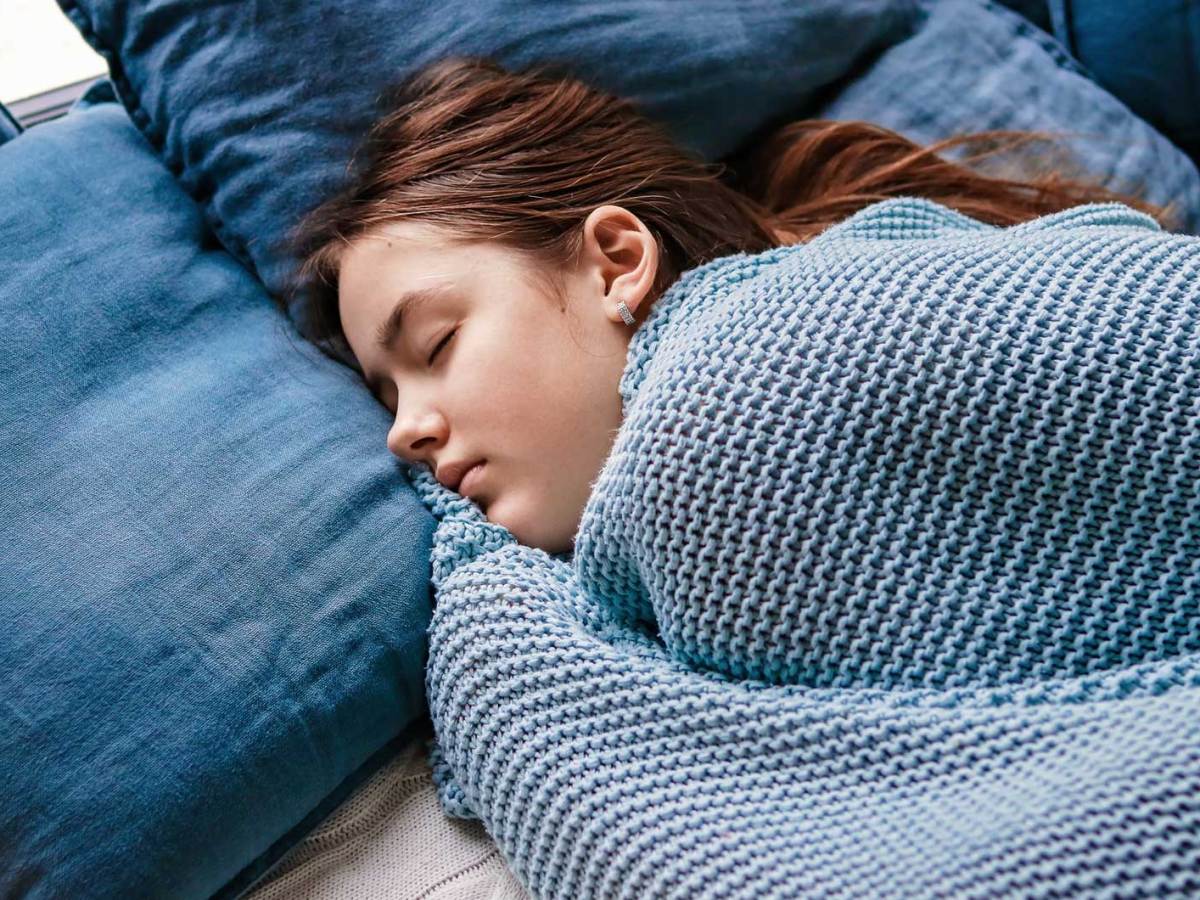 Mädchen im Teenageralter liegt im Bett, zugedeckt mit einer leichten Decke.