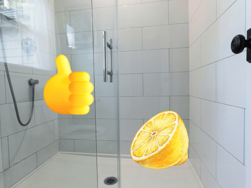 Helle geflieste Duschkabine mit Glaswand, Zitronenhälfte und Daumen-hoch-Emoji als Symbol für natürliche Reinigung.