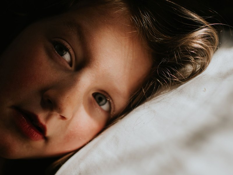 Nahaufnahme eines Mädchens. Sein Kopf liegt auf einem weißen Kissen.