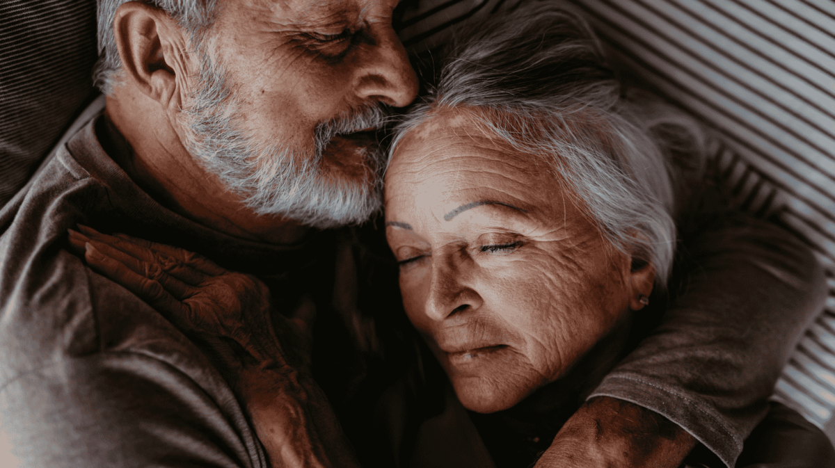 Älteres Paar liegt im Bett und kuschelt.
