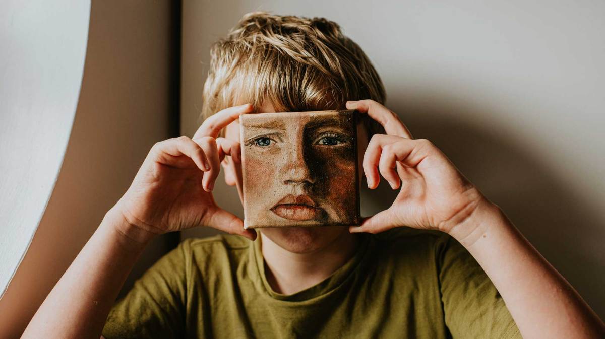 Junge hält sich ein kleines Ölgemälde von sich selbst vors Gesicht.