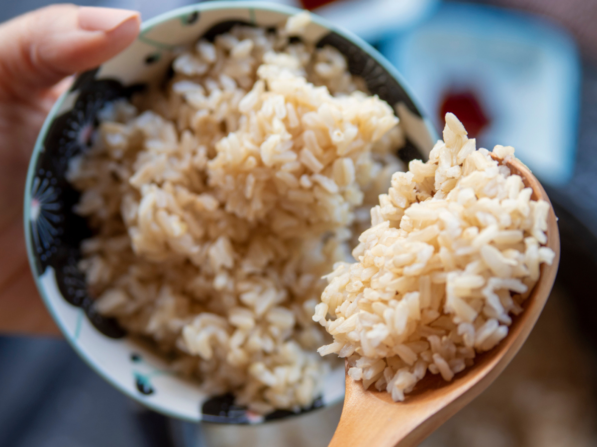 Person hält eine Schale und einen Holzkochlöffel mit Reis in den Händen.