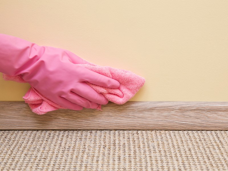 Frau trägt pinkfarbene Handschuhe zum Putzen der Fußleisten mit einem blauen Tuch