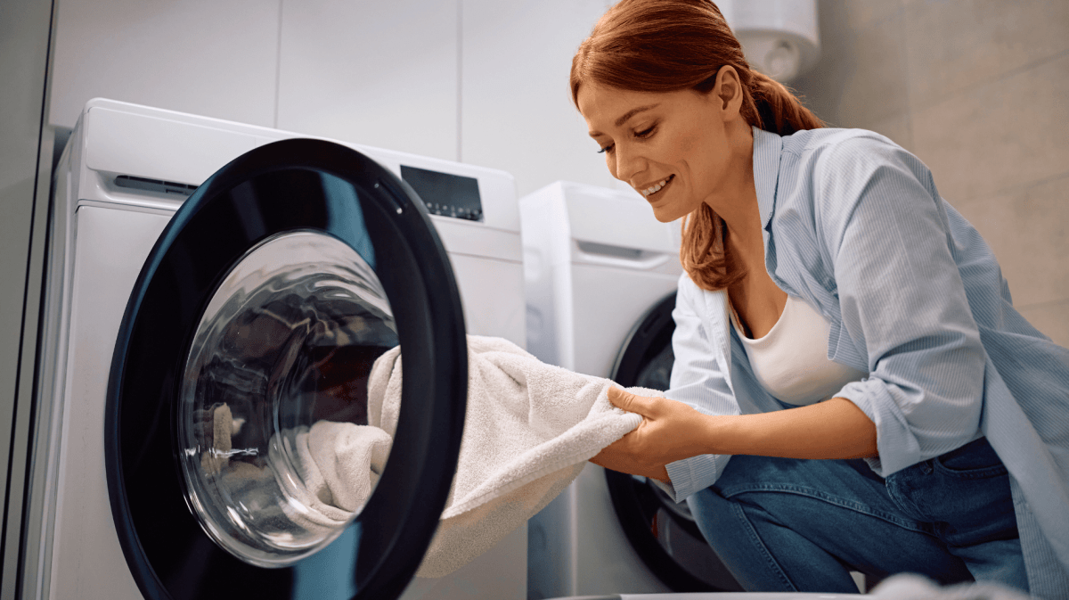 Rothaarige Frau nimmt weißes Handtuch aus ihrer Waschmaschine.