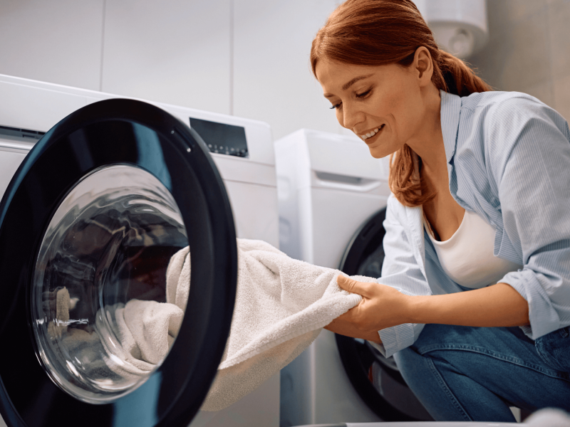 Rothaarige Frau nimmt weißes Handtuch aus ihrer Waschmaschine.