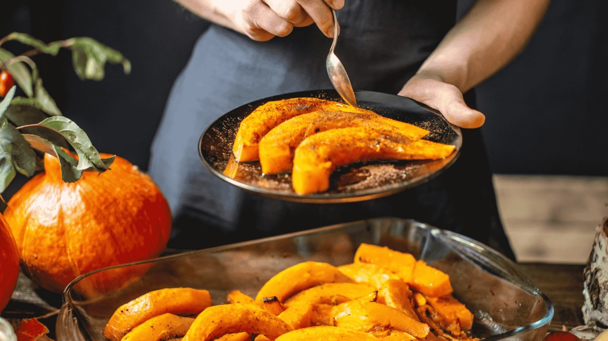 Köchin hält Scheiben von gebackenem orange Hokkaido-Kürbis mit Honig und Zimt. Herbstliches Essen in einer gemütlichen Küche.