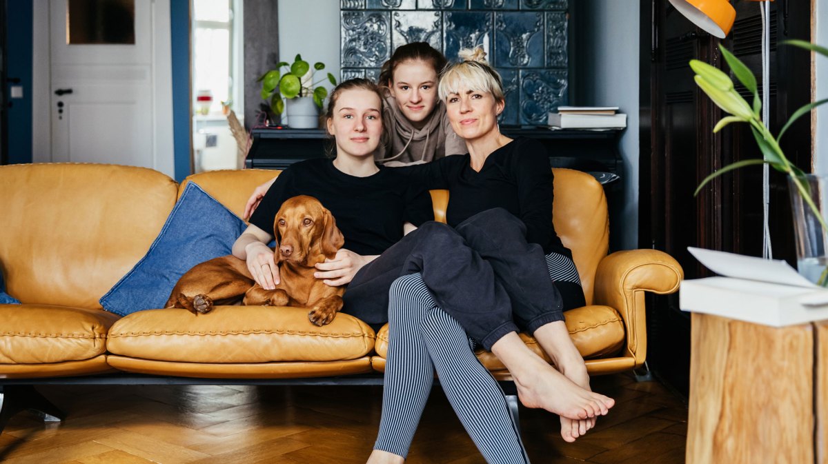 Mutter mit zwei Teenager Töchtern auf Sofa mit Hund